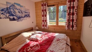 A bedroom with a wooden headboard, a bed with a red and white patterned bedspread, and a window with patterned curtains.