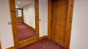 A narrow hallway with wooden doors and a red patterned carpet.