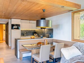 A modern kitchen with a central island, a dining area with a bench, and a large window.
