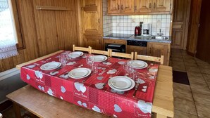 Ett kök med träskåp, kakel ovanför arbetsbänken och ett matbord för fyra personer, täckt med en röd duk.