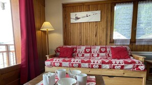 Ett mysigt rum med en soffa i trä som är dekorerad med röda och vita hjärtmönster, ett träbord med vita koppar och fat samt en lampa till vänster.