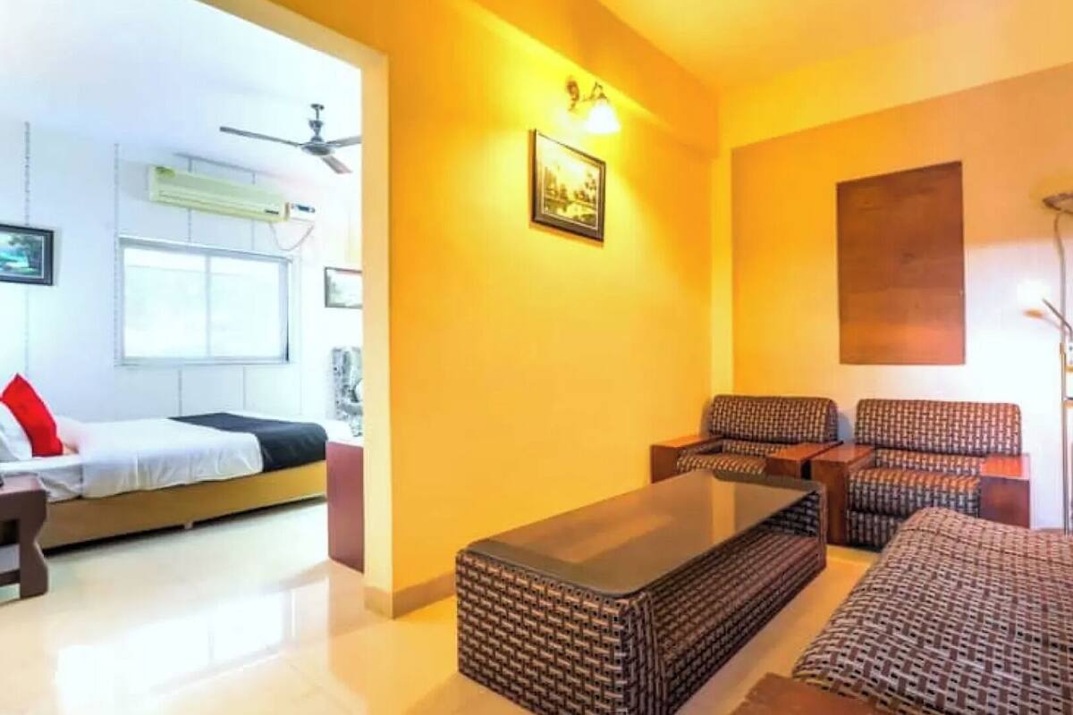 A living room with a sofa set, a coffee table, and a bed with a red pillow.