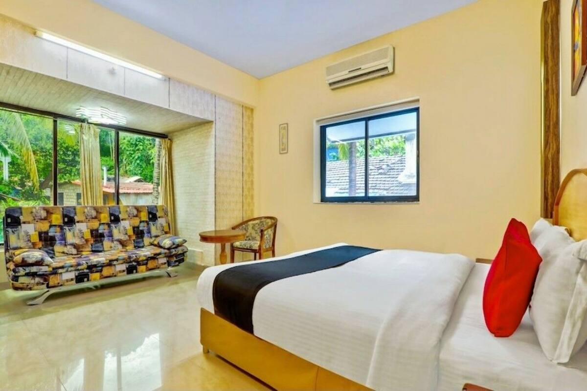 A hotel room with a bed, a sofa, a small table, and a window with a view of greenery.
