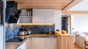 A modern kitchen with a wooden ceiling, built-in cabinets, a black countertop, and a small wooden island with a bowl of fruit.