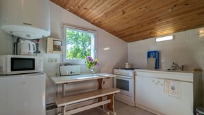A compact kitchen with a wooden ceiling, a window with a view of trees, a microwave, a kettle, a stove, and a sink. - Guest rooms with garden near Loire castles (Châtillon-sur-Indre)