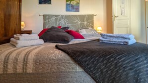 A neatly made bed with pillows and folded towels, a wooden headboard, and a wall with framed pictures. - Guest rooms with garden near Loire castles (Châtillon-sur-Indre)