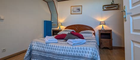 Un llit ben fet amb roba de llit estampada, dues làmpades de nit, un quadre al mur i una porta blava.
