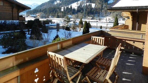 A wooden deck with a table and chairs overlooking a snowy landscape with mountains in the background.