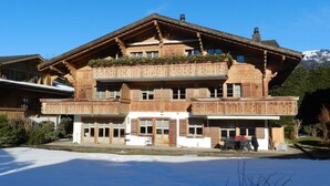 A large, multi-story chalet with a wooden facade, balconies, and a ski slope in the background.