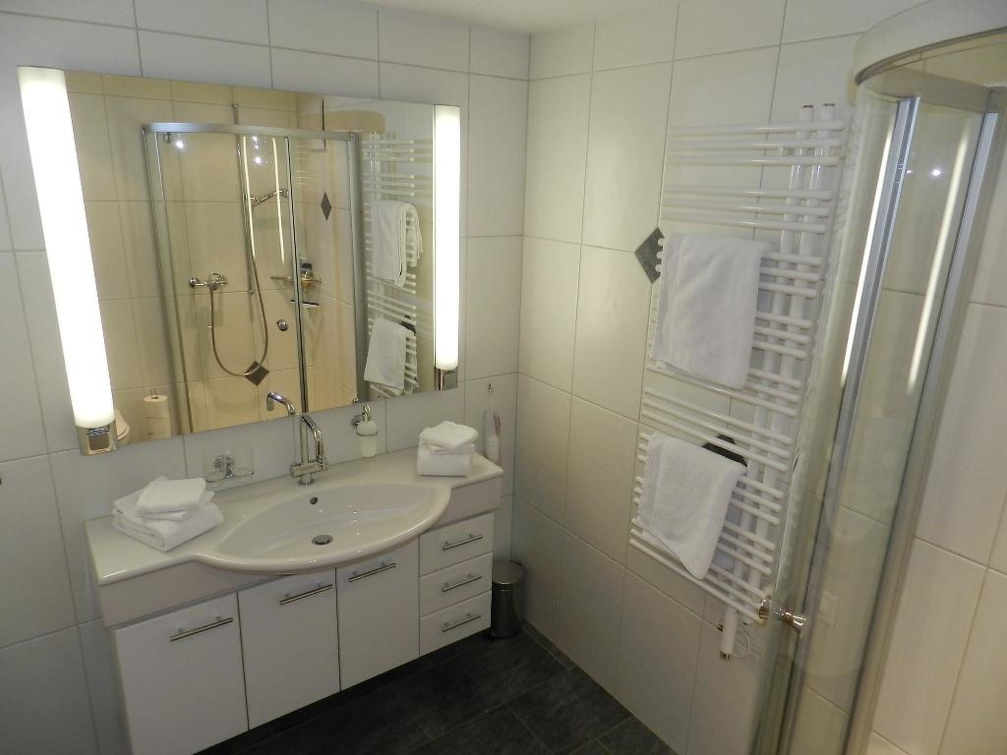 A modern bathroom with a glass-enclosed shower, a large mirror, and a white vanity with a sink and towel rack.