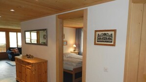 A wooden cabin interior with a large mirror, a wooden dresser, a bed, and a framed picture on the wall.
