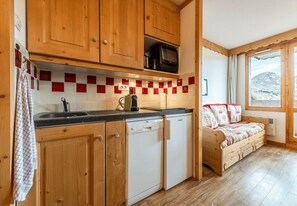 A compact kitchen with wooden cabinets, a dishwasher, and a microwave. There is a window with a view of a mountain. - Smartstay Themis - Belle Plagne (Belle-Plagne)