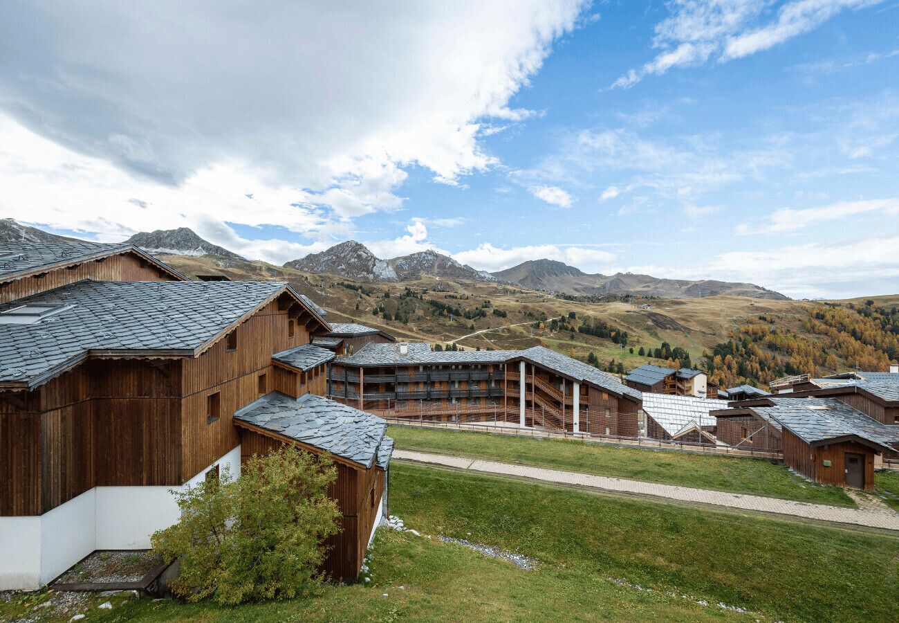 A traditional wooden building complex with multiple chalet-style lodges, set against a backdrop of mountains and clear skies.
