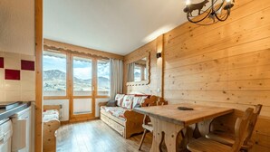 Un interior de fusta amb una taula de menjador, cadires, un sofà i una zona de cuina amb un frigorífic.