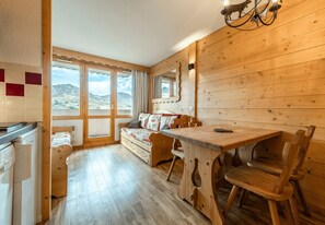 A wooden interior with a dining table, chairs, a sofa, and a kitchen area with a refrigerator. - Smartstay Themis - Belle Plagne (Belle-Plagne)