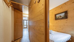 Un interior de fusta amb un llit, una porta de fusta i un passadís que condueix a una habitació.