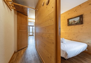A wooden interior with a bed, a wooden door, and a hallway leading to a room. - Smartstay Themis - Belle Plagne (Belle-Plagne)