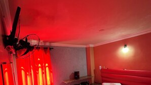 Hotellihuone, jossa on sänky, työpöytä, tuoli ja lattiatuuletin.
