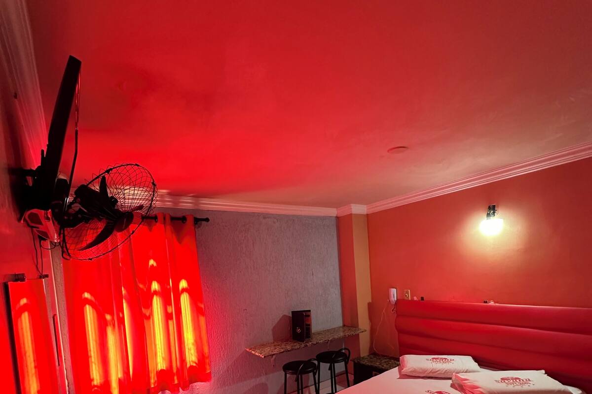 A hotel room with a bed, a desk, a chair, and a standing fan.