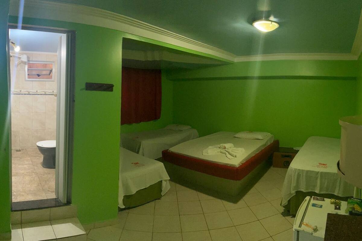 A small, green-walled room with a single bed, a bedside table, a mirror, and a window.