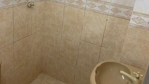 Kylpyhuone, jossa on beigenväriset laatat, wc-istuin, pesuallas ja suihkutila.