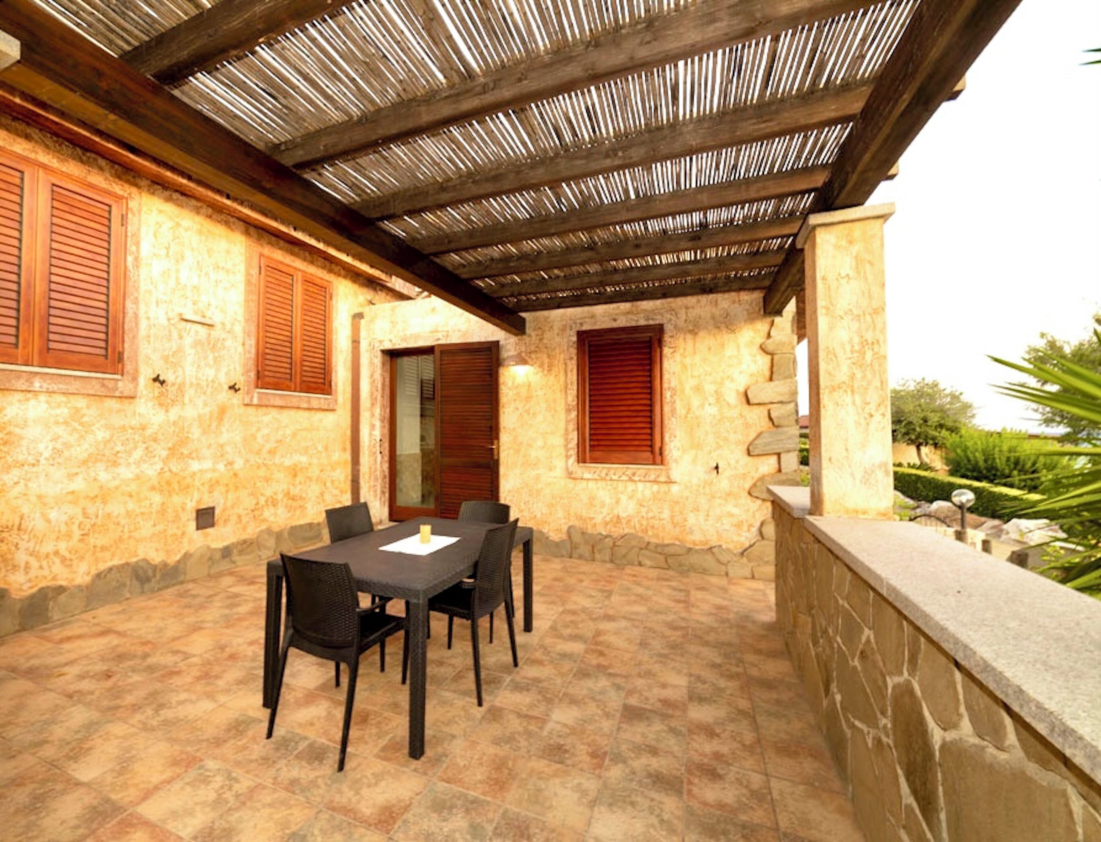 Eine Außenpatio mit Steinboden, einem Tisch und Stühlen sowie einer Holzhütte darüber.