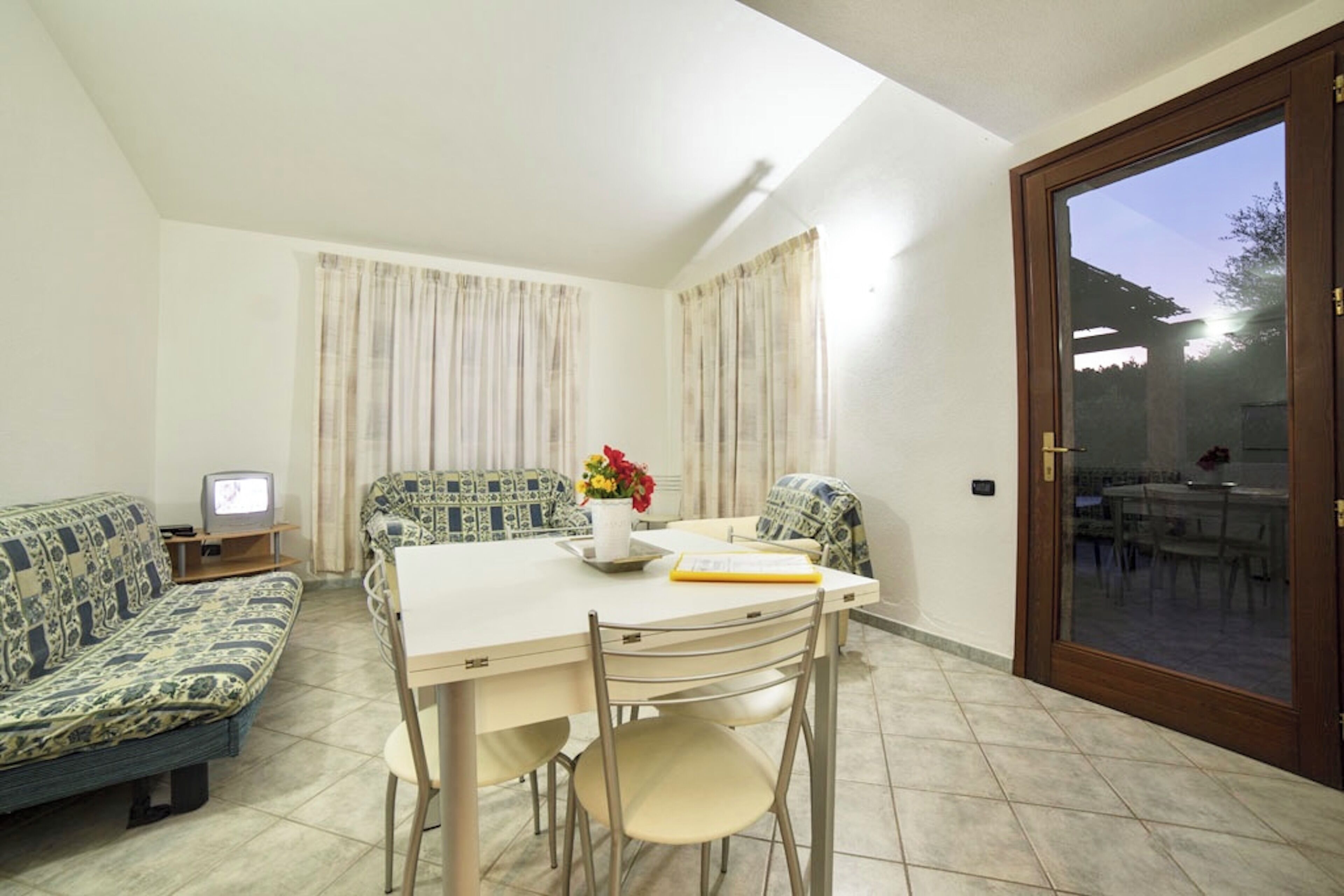 A dining area with a table, chairs, a sofa, a TV, and curtains.