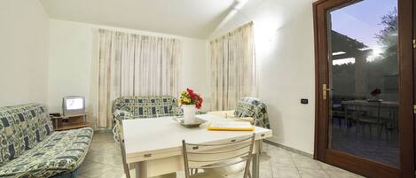 A dining area with a table, chairs, a sofa, a TV, and curtains.