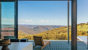 A modern room with a large glass door leading to a scenic view of rolling hills and a clear sky. - Mountain Top Bilpin, Studio 2 (Bilpin)