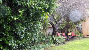 A backyard with a large tree, a wooden fence, and a seating area with red chairs.