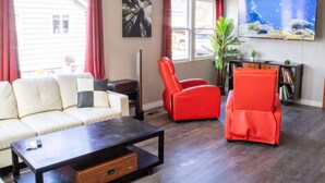 A living room with a sofa, two red chairs, a coffee table, a TV, and a bookshelf.