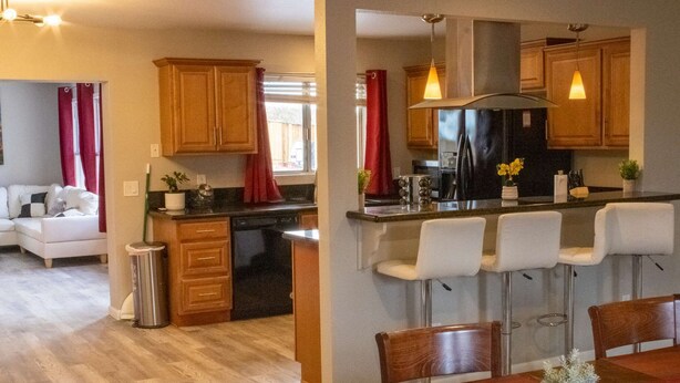 Una cocina moderna con armarios de madera, un refrigerador negro y una zona de bar con taburetes blancos.