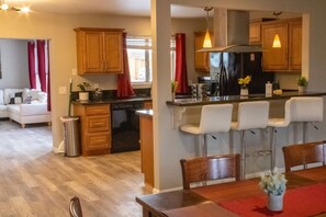 A modern kitchen with wooden cabinets, a black refrigerator, and a bar area with white bar stools. - The Joshua Tree Forest:FREE* Heated Salt Pool,City&Mtn.Views,BBQ,1/2 ACRE,Billiards,Board Games! (Twentynine Palms)