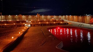 Un área de piscina al aire libre de noche, con bancos de madera e iluminación a lo largo del perímetro.