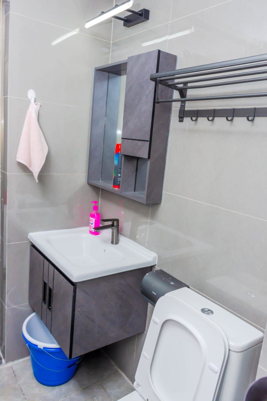 A modern bathroom with a white sink, a mirror cabinet, a towel rack, and a toilet.