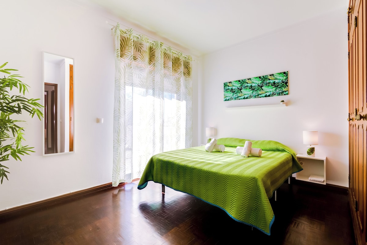 A hotel room with a bed, a nightstand, a lamp, a window with curtains, and a wall-mounted picture.