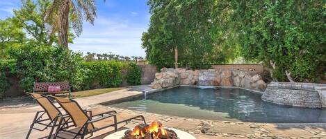 A pool area with a fire pit, lounge chairs, and a stone wall.