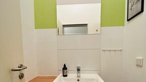 A small bathroom with a white sink, a wooden countertop, a mirror above the sink, and a small trash bin. - House Rasink I Fitters I 160m2 (Ibbenbüren)