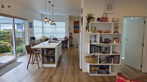 Eine moderne Küche mit einer zentralen Kochinsel, einem Essbereich mit Stühlen und einem Bücherregal mit Büchern und Dekorationsobjekten.