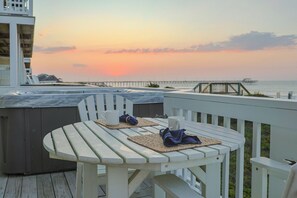 A wooden deck with a hot tub and two tables, one with a napkin and a mug. - Ocean Echos – Luxury Oceanfront Vacation Rental in North Topsail Beach (North Topsail Beach)
