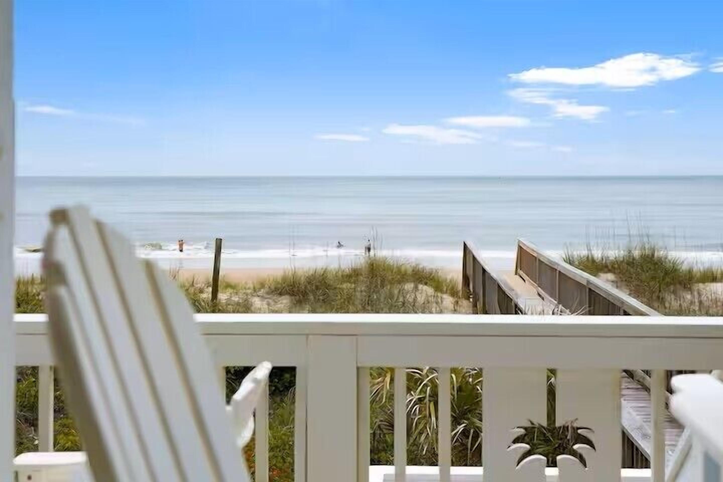A beach view from a balcony with a white railing and a chair.
