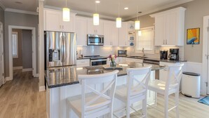 A modern kitchen with white cabinetry, stainless steel appliances, and pendant lighting. - Ocean Echos – Luxury Oceanfront Vacation Rental in North Topsail Beach (North Topsail Beach)