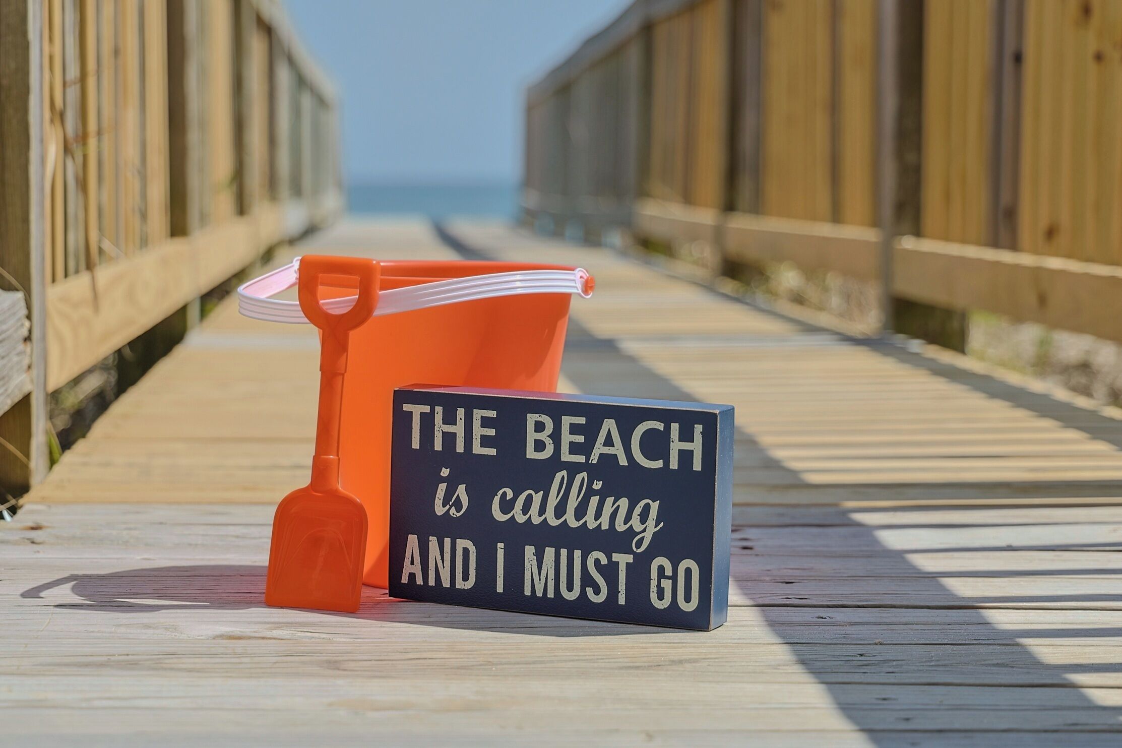A wooden boardwalk with a sign that reads 'The beach is calling and I must go.'