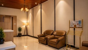A reception area with a wooden reception desk, a standing lamp, two leather chairs, a floor lamp, and a bulletin board. - Hotel Unnati Stay Inn Vijayapura By HRG (Bijapur)