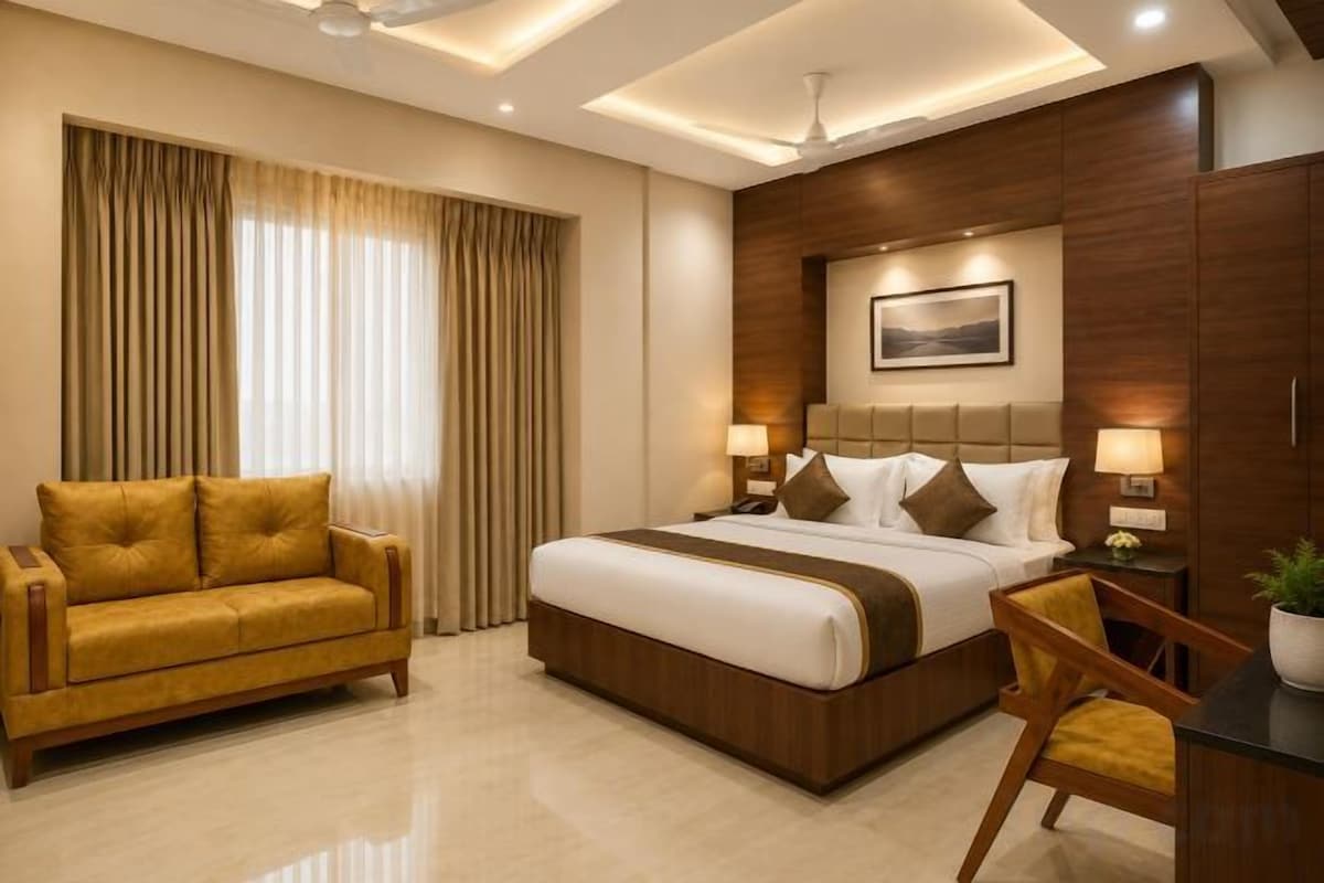 A hotel room with a large bed, a sofa, a desk, and a chair.