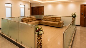 A modern lobby with a sectional sofa, a glass railing, and a decorative vase. - Hotel Unnati Stay Inn Vijayapura By HRG (Bijapur)