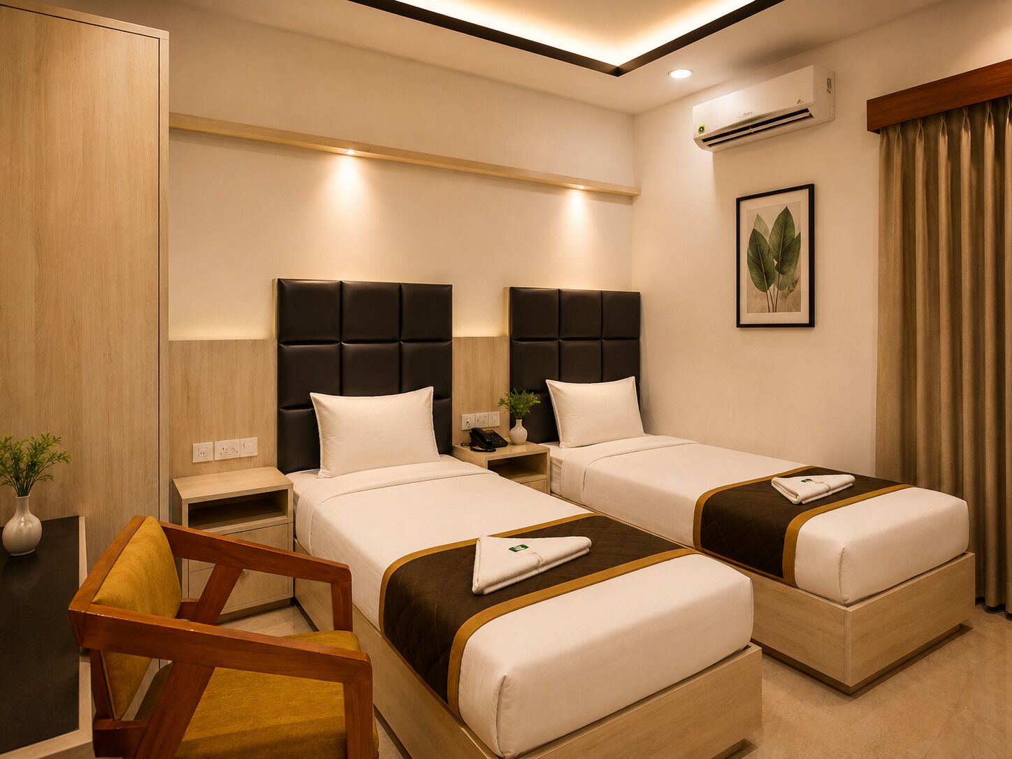 A hotel room with two beds, a desk, a chair, an air conditioning unit, and a framed plant on the wall.