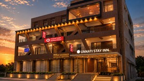 A multi-story hotel with a modern design, featuring a prominent sign for 'UNNATI STAY INN' and a sign for 'Muthoot Finance.' - Hotel Unnati Stay Inn Vijayapura By HRG (Bijapur)