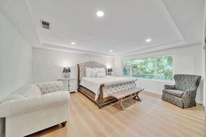 Relax in this serene bedroom with a large bed, two armchairs, and a bench, offering a peaceful view of the surrounding greenery.
