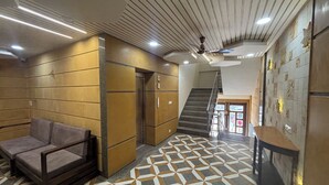 Un vestíbulo con piso de diseño geométrico, un sofá, un ascensor, una escalera y una pared con azulejos decorativos.